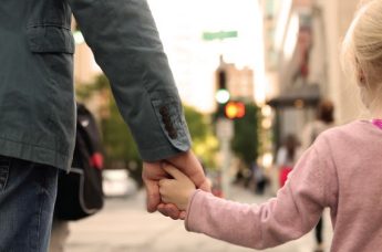 Adult holding child's hand while walking down the street.  
